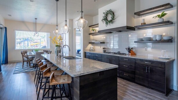 Una cucina moderna con isola centrale, mobili scuri e illuminazione a sospensione.