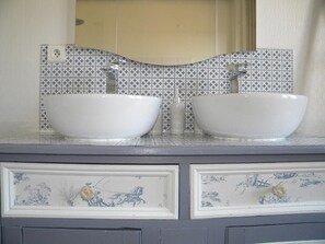 Un baño con dos lavamanos blancos tipo sobreencimera, un espejo encima y baldosas con diseño en la pared.