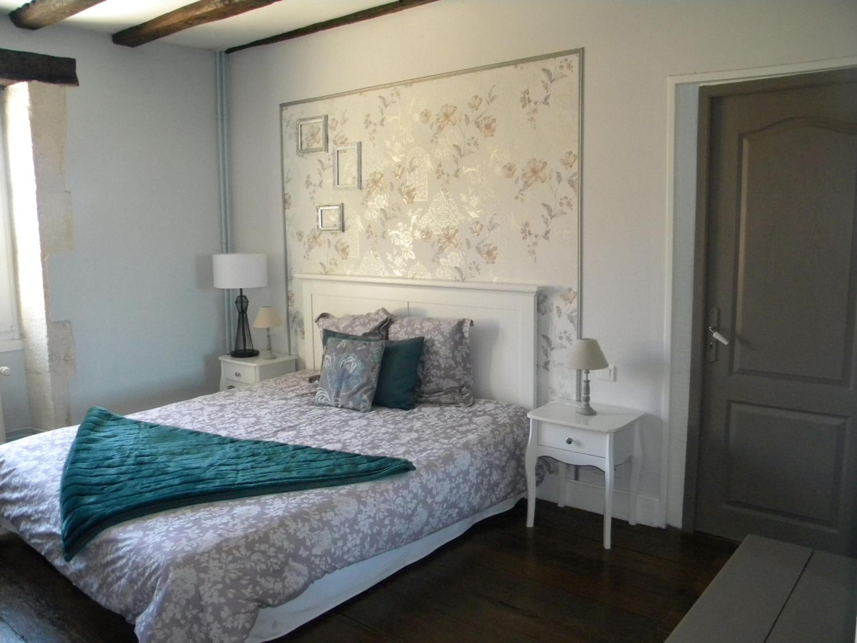 Une chambre à coucher avec un lit, deux tables de chevet, une porte et un mur recouvert d’un papier peint à motifs floraux.