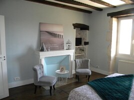 Una habitación con chimenea, dos sillones, una cama con una manta verde y un cuadro en la pared.