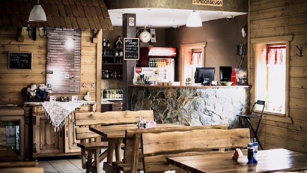 A rustic wooden interior with a stone wall, wooden tables and benches, a menu board, and a sign reading "SAMOBIEŚUGA". - Motel w Lace (Boleslawiec)
