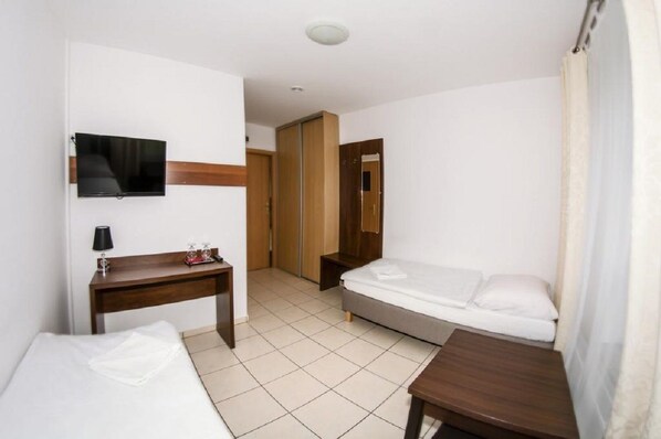 Quarto de hotel com cama, escrivaninha, televisão e armário.