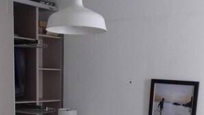 A bedroom with a bed, a white hanging lamp, a wardrobe, and a framed picture on the wall.