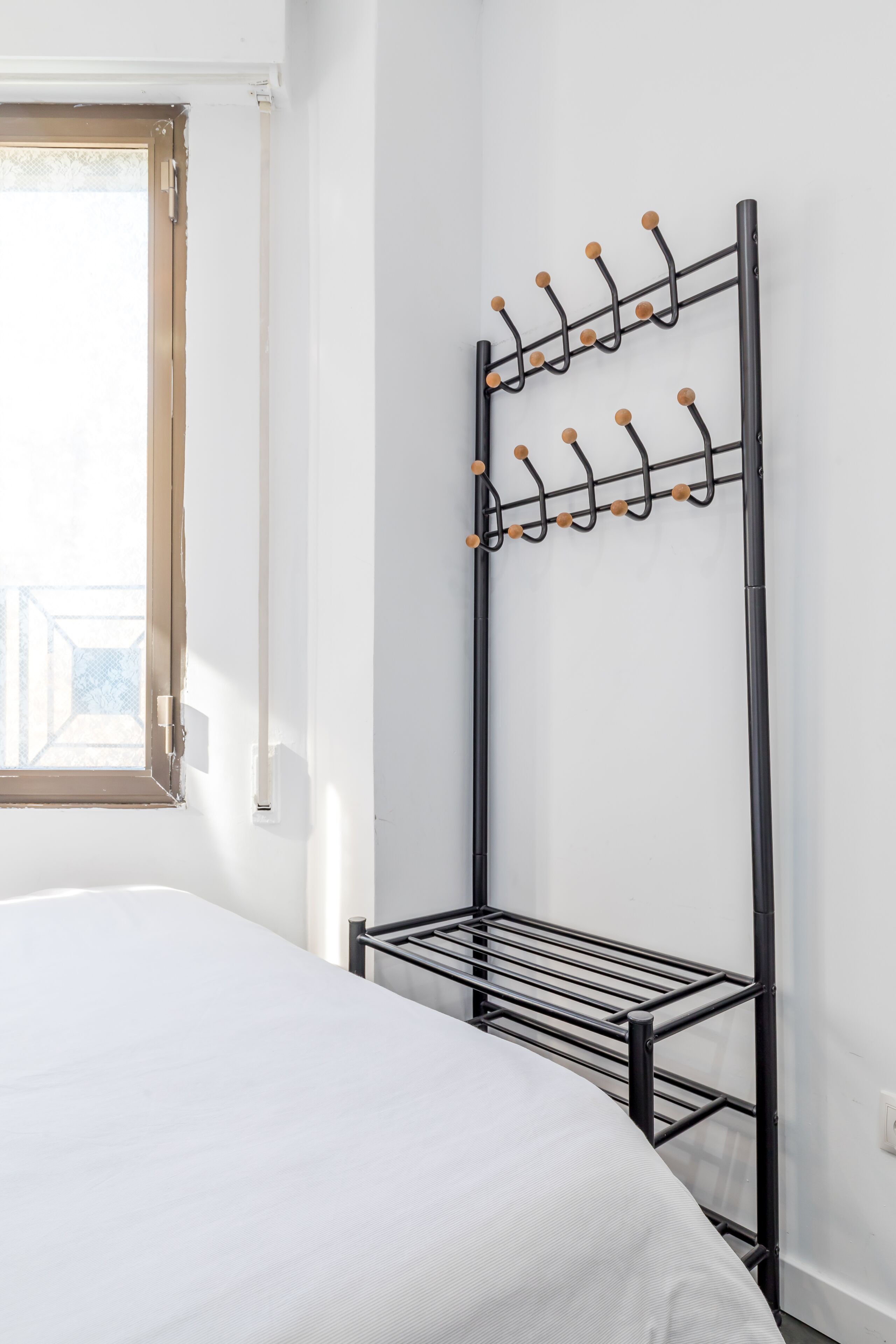 A room with a bed, a black metal drying rack with hooks, and a window with a view.