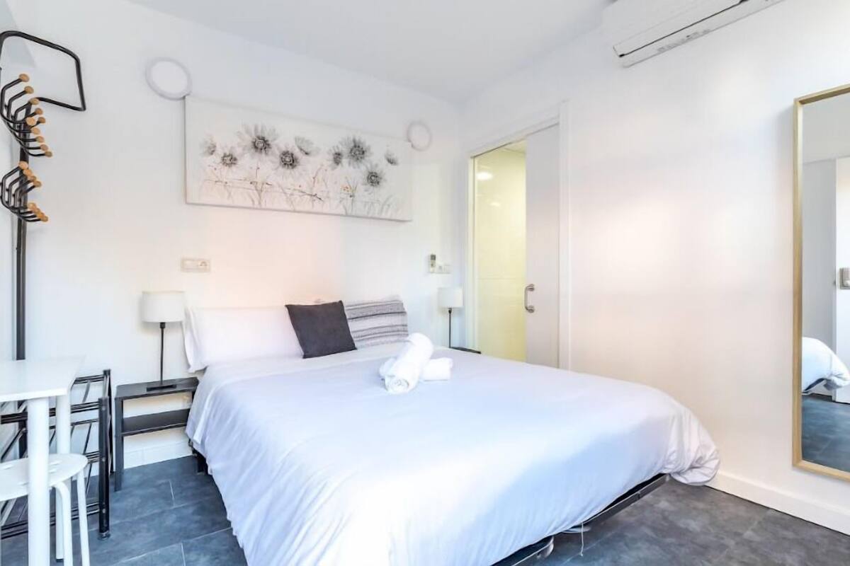 Ein modernes Hotelzimmer mit einem großen Bett, einem Schreibtisch und einem Stuhl. Ein Gemälde hängt an der Wand und ein Spiegel befindet sich rechts.
