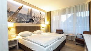 A hotel room with a large bed, a desk, a chair, and a painting of a bridge and sailboats on the wall. - Hotel Spiekeroog (Spiekeroog)