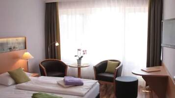 Une chambre d’hôtel avec un lit, deux chaises, une petite table avec un vase et un téléviseur fixé au mur.
