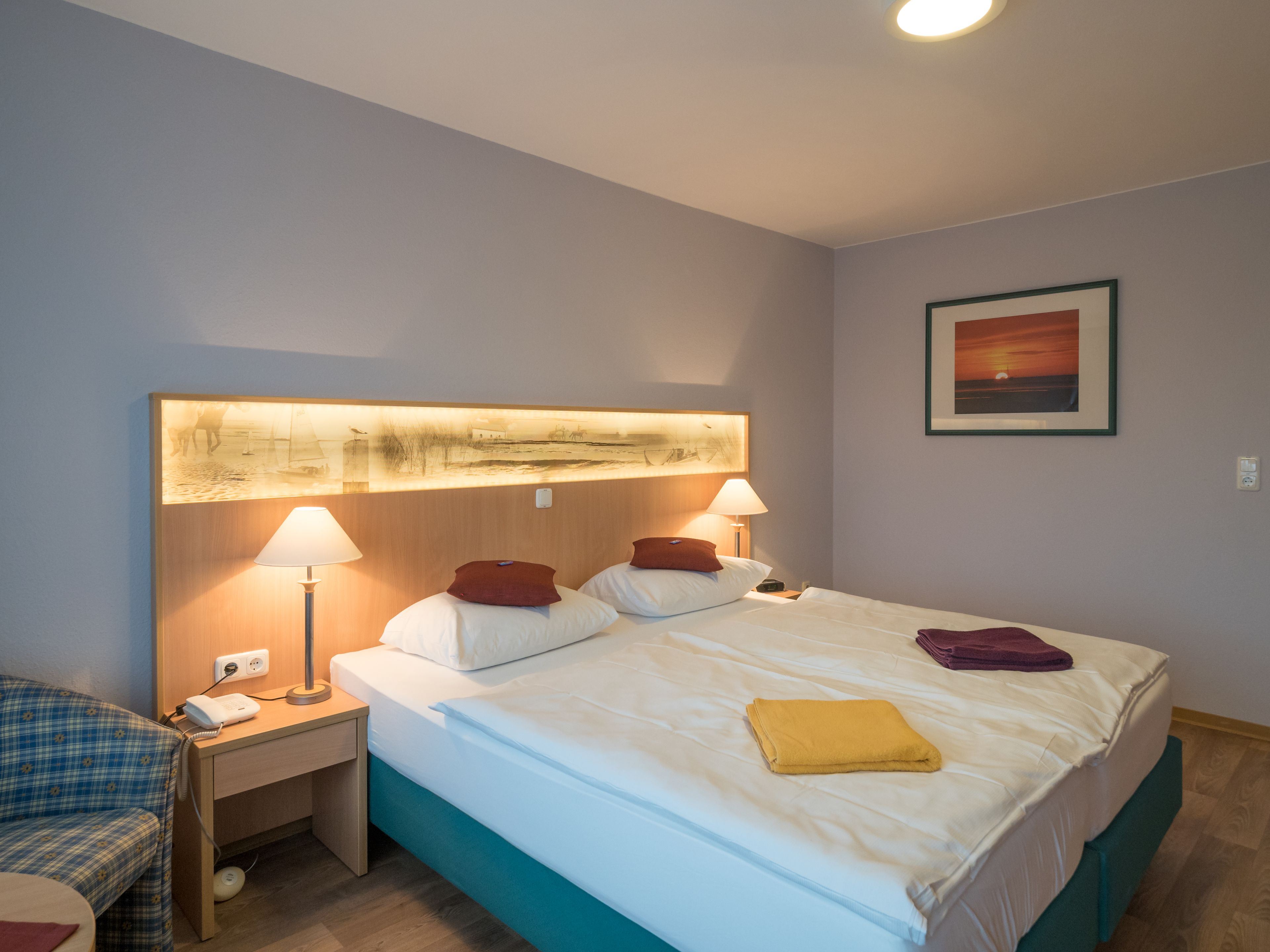 Une chambre d’hôtel avec un lit, deux lampes de chevet, une table de chevet, un bureau, une chaise et un tableau encadré au mur.