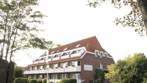 A multi-story building with a red brick facade, multiple windows, and a balcony with flower boxes. - Hotel Spiekeroog (Spiekeroog)