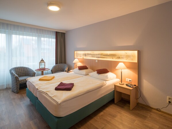 Une chambre d’hôtel avec un grand lit, deux chaises, une petite table et une lampe.