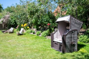 Um jardim com churrasqueira, espreguiçadeiras e diversas plantas.