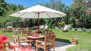 An outdoor patio area with wooden furniture, a table, and a large umbrella. - Hotel Spiekeroog (Spiekeroog)