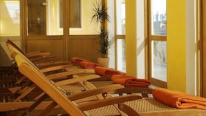 A sun lounger with a view of a garden through large windows. - Hotel Spiekeroog (Spiekeroog)