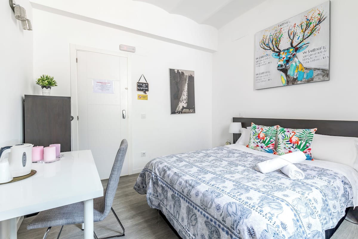 Una habitación de hotel con una cama, un escritorio, una silla, una mesita con velas y un cuadro en la pared.