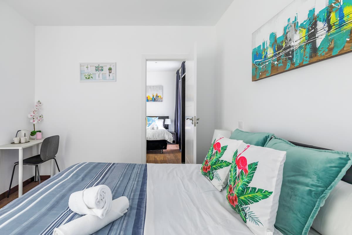 Una habitación de hotel con cama, escritorio, silla y un cuadro en la pared.