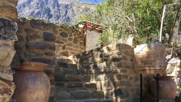 A stone staircase leading to a wooden pergola with a sign for Casa Blanca Lodge, featuring stone walls and terracotta pots.