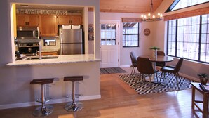 A kitchen with wooden cabinets, a stainless steel refrigerator, and a sign that reads "THE WHITE MOUNTAINS". There are two bar stools and a dining table with chairs. - Luxury Cabin Retreat with Hot Tub on Spacious Wooded Lot (Pinetop)