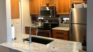 A kitchen with wooden cabinets, stainless steel appliances, a granite countertop, and a sign reading "THE WHITE MOUNTAINS". - Luxury Cabin Retreat with Hot Tub on Spacious Wooded Lot (Pinetop)