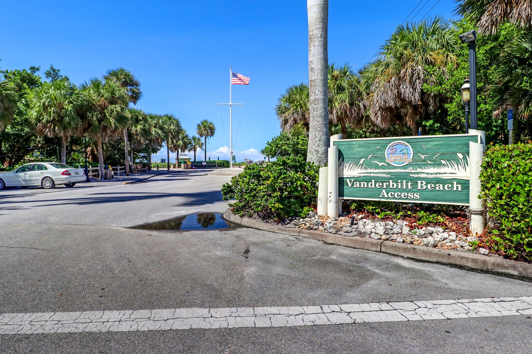 A road sign for Vanderbilt Beach Access with a clear sky and palm trees in the background.