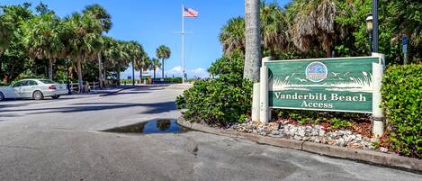 A road sign for Vanderbilt Beach Access with a clear sky and palm trees in the background.