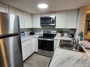 A kitchen with white cabinets, a stainless steel refrigerator, a microwave, an oven, and a sink with a faucet.