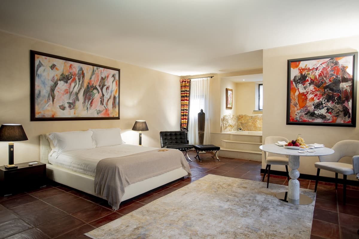 A hotel room with a large bed, a desk, a chair, and two paintings on the walls.