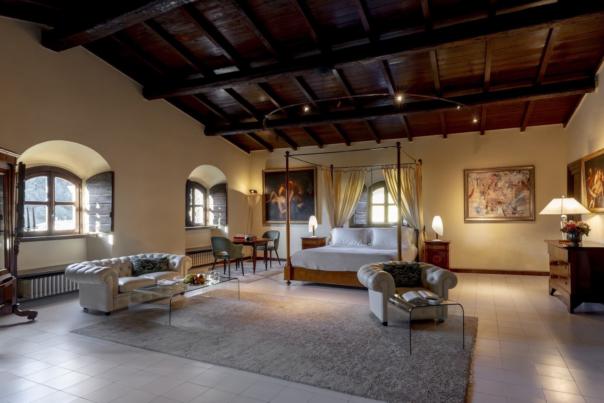 A spacious bedroom with a four-poster bed, a sitting area with a sofa and armchairs, and a dining area with a table and chairs.