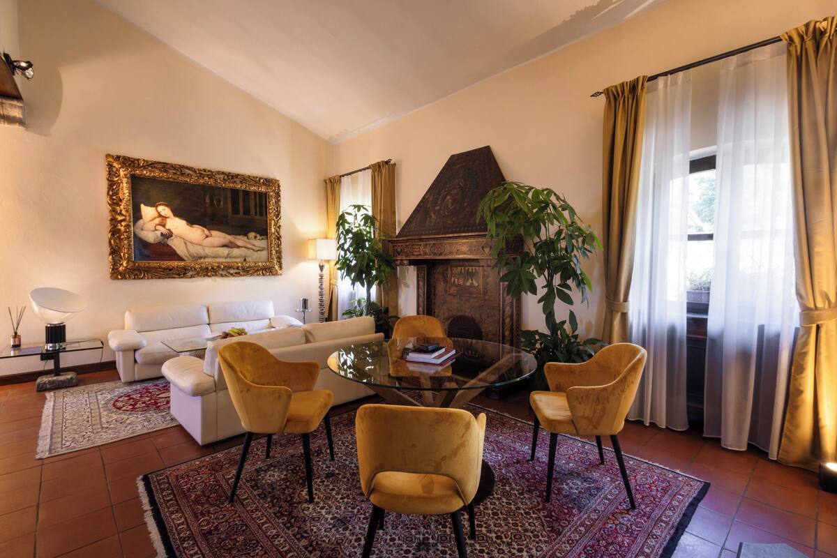 A living room with a sofa, armchairs, a glass coffee table, a fireplace, and a painting on the wall.