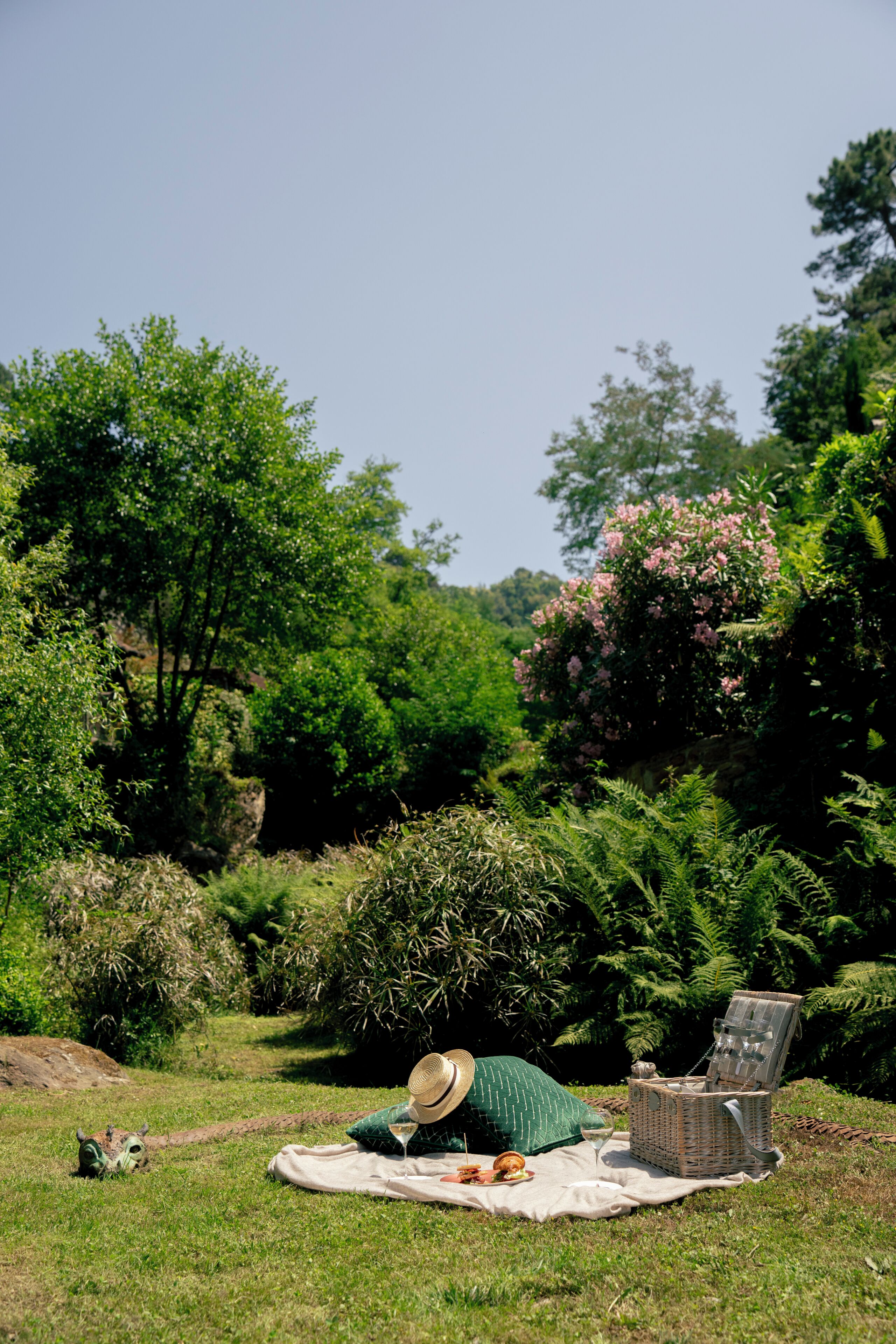 Un montaje para picnic en un jardín exuberante, con una manta, una silla de mimbre y una cesta de picnic.