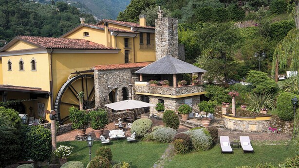 A historic building with a water wheel, stone tower, and outdoor seating area surrounded by lush gardens. - Il Bottaccio, Relais & Chateaux (Montignoso)