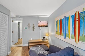 A modern living room with a grey sofa, a wooden coffee table, and a TV mounted on the wall. - Heated Pool, Mini Golf, Walk to Beach, Beach Gear (St Augustine)