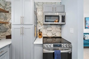 A compact kitchen with white cabinets, a microwave, and a stove. - Heated Pool, Mini Golf, Walk to Beach, Beach Gear (St Augustine)
