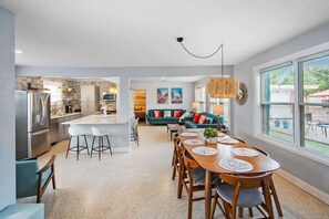 A modern kitchen with a central island, a dining area with a long table, and a living room with a sofa and a coffee table.
