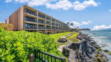 A hotel with multiple balconies, a well-maintained lawn, and a view of the ocean.