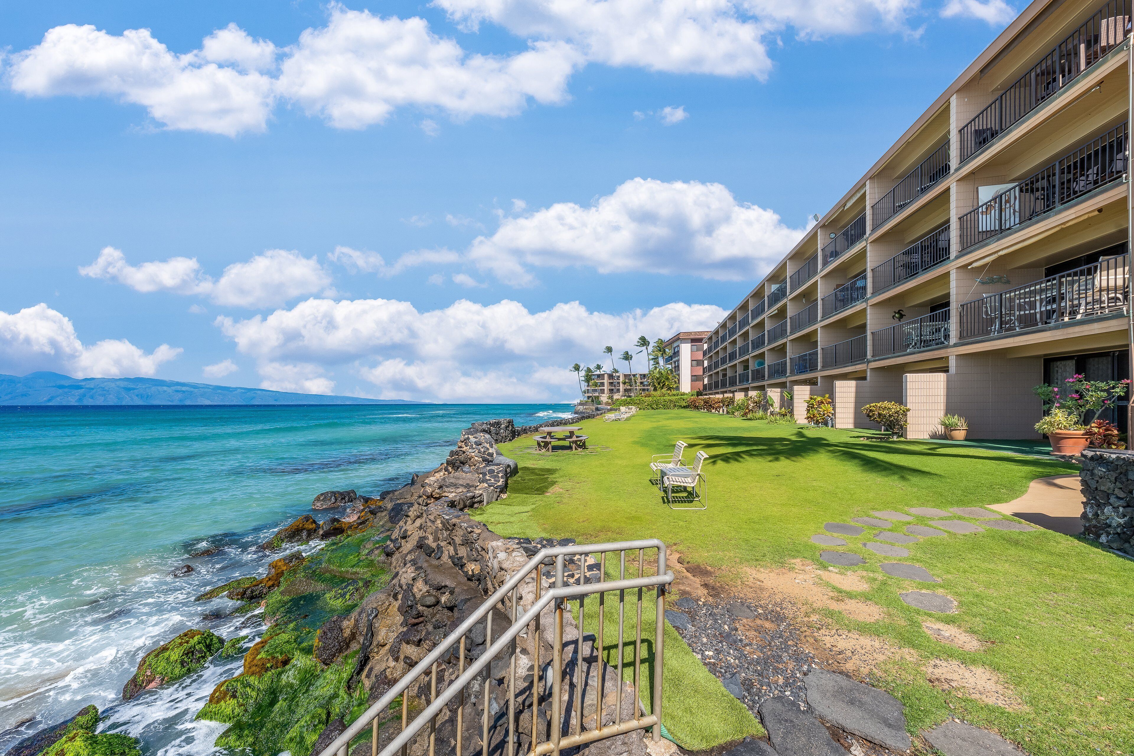 A hotel with a pool area, a view of the ocean, and a well-maintained lawn.
