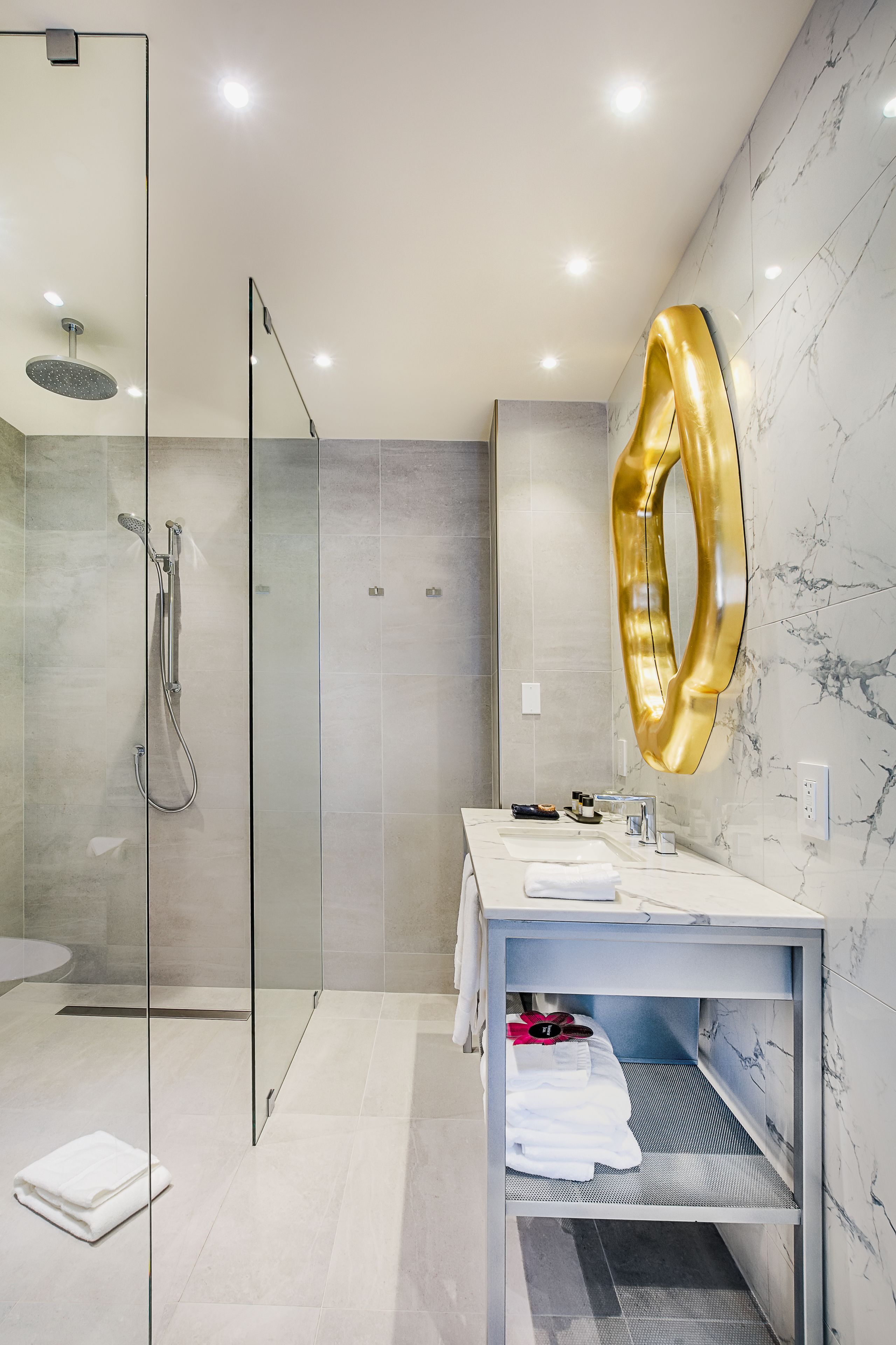 A modern bathroom with a glass-enclosed shower, a marble-tiled wall, and a vanity with a gold mirror.