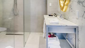 A modern bathroom with a glass-enclosed shower, a marble-tiled wall, and a vanity with a gold mirror.