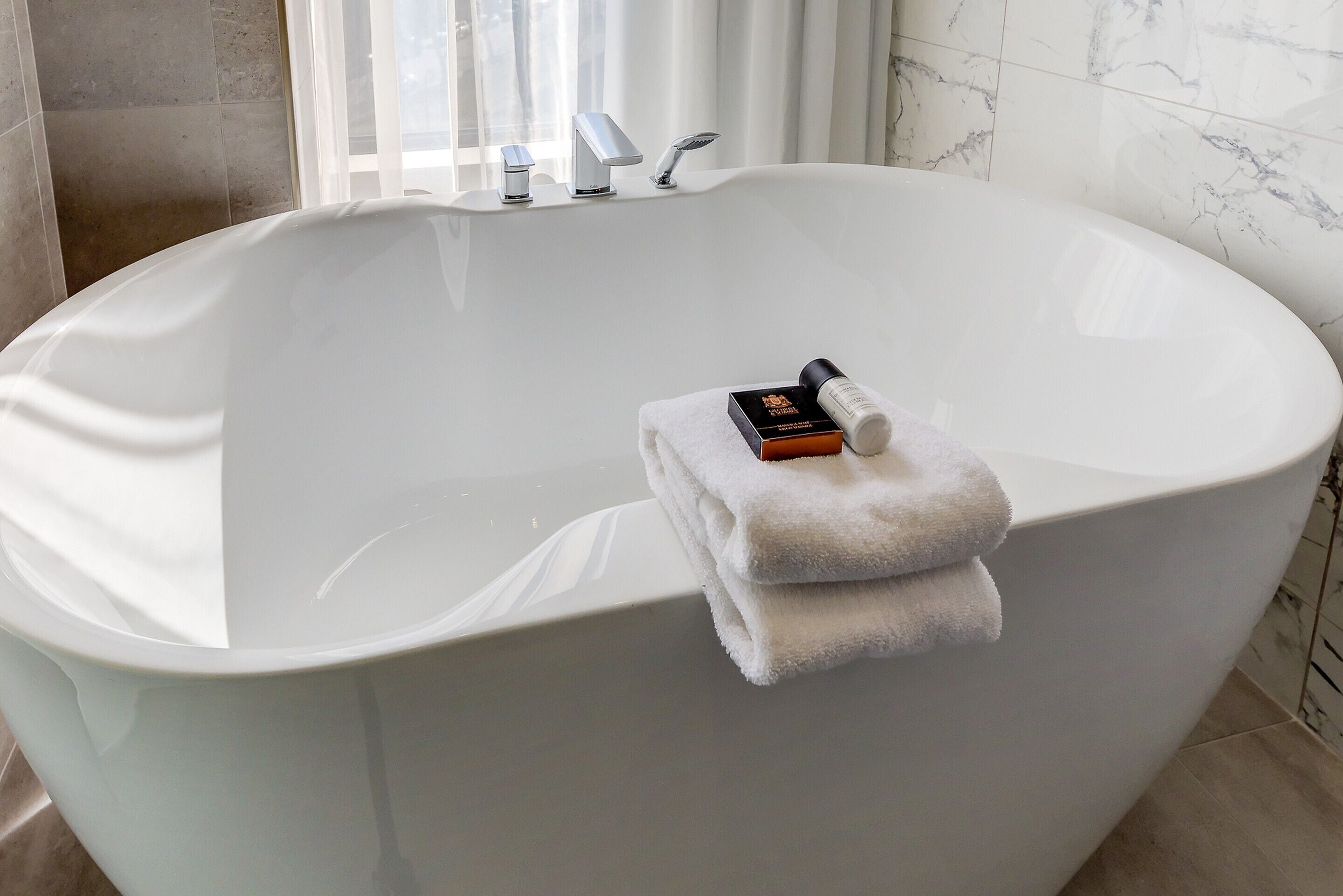 Eine große, freistehende Badewanne mit Handtuch und Flasche darauf.