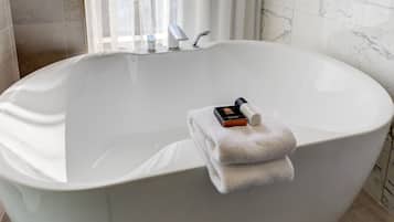 Eine große, freistehende Badewanne mit Handtuch und Flasche darauf.