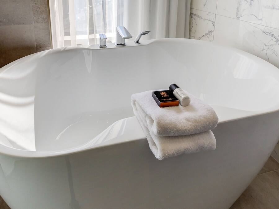 Eine große, freistehende Badewanne mit Handtuch und Flasche darauf.