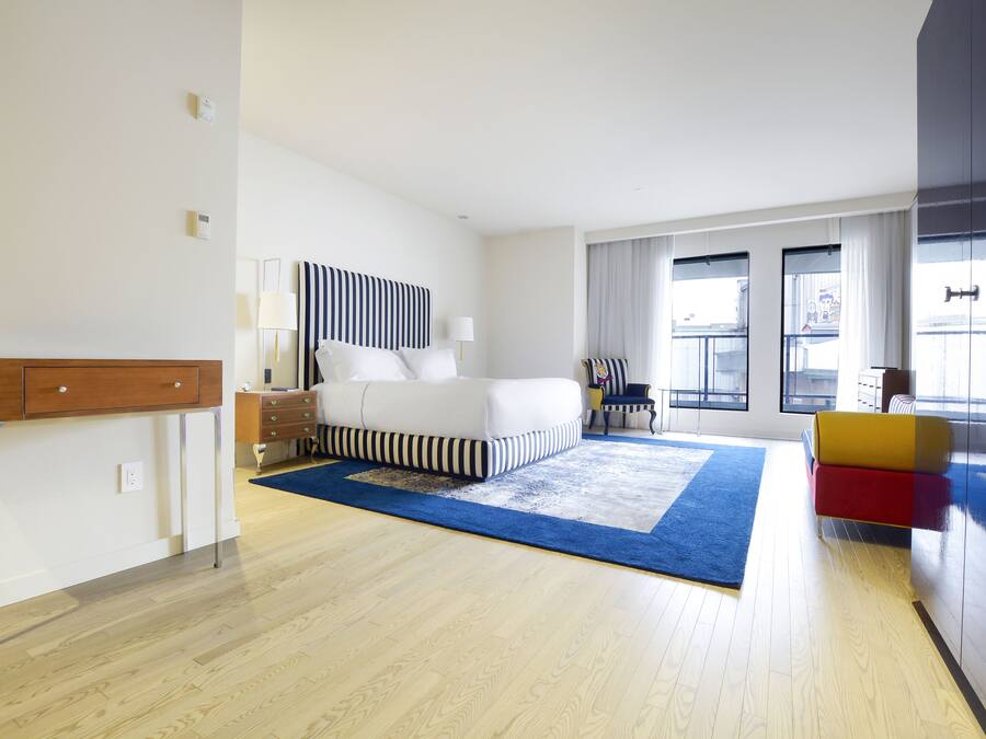 Una habitación de hotel moderna con una cama grande, un escritorio y una silla. Hay ventanas con cortinas y vistas al exterior.