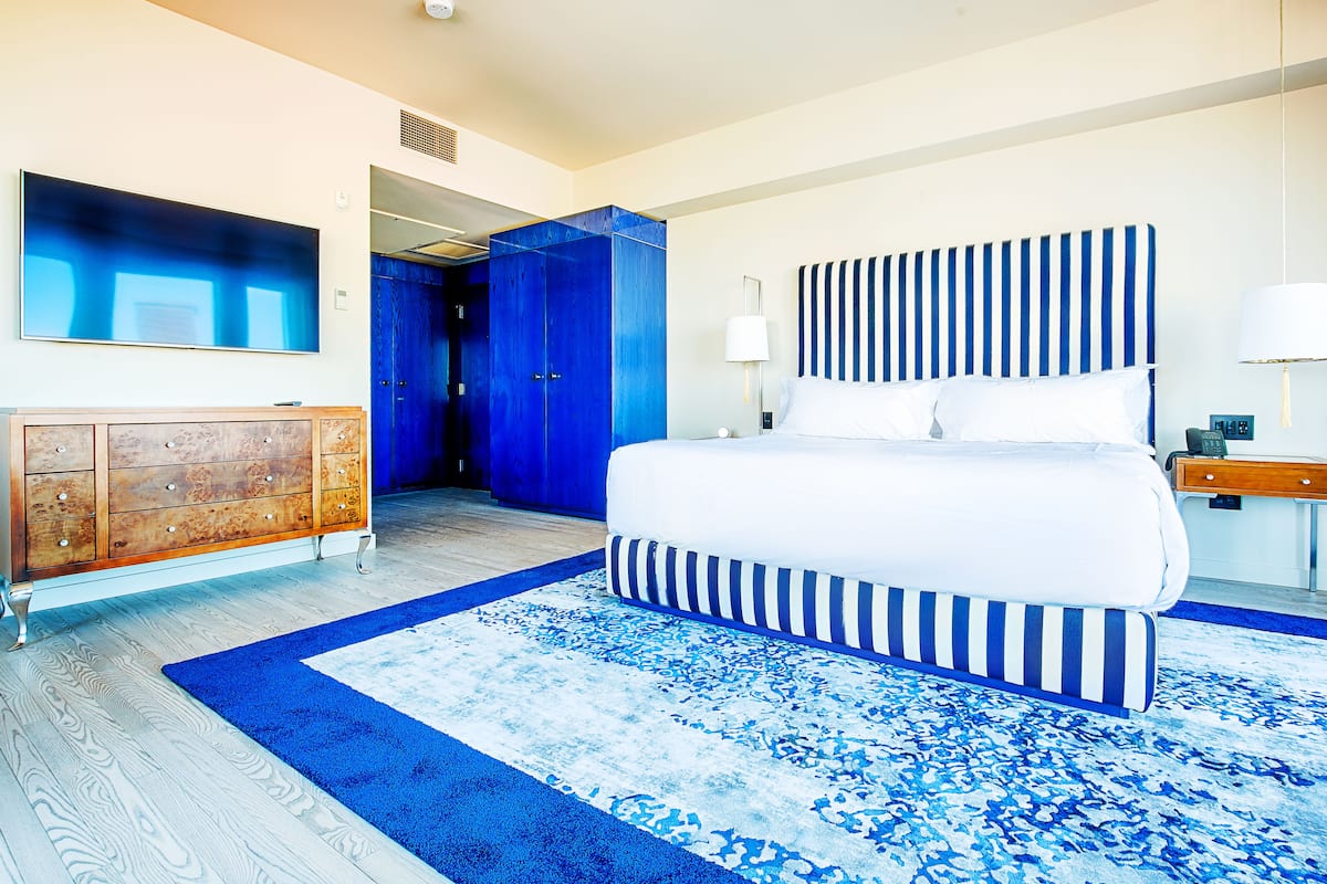 A bedroom with a large bed, a wooden dresser, a blue and white patterned rug, and a blue door.