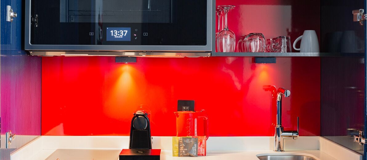 Una cocina con salpicadero rojo, una cafetera, un hervidor y un lavabo.