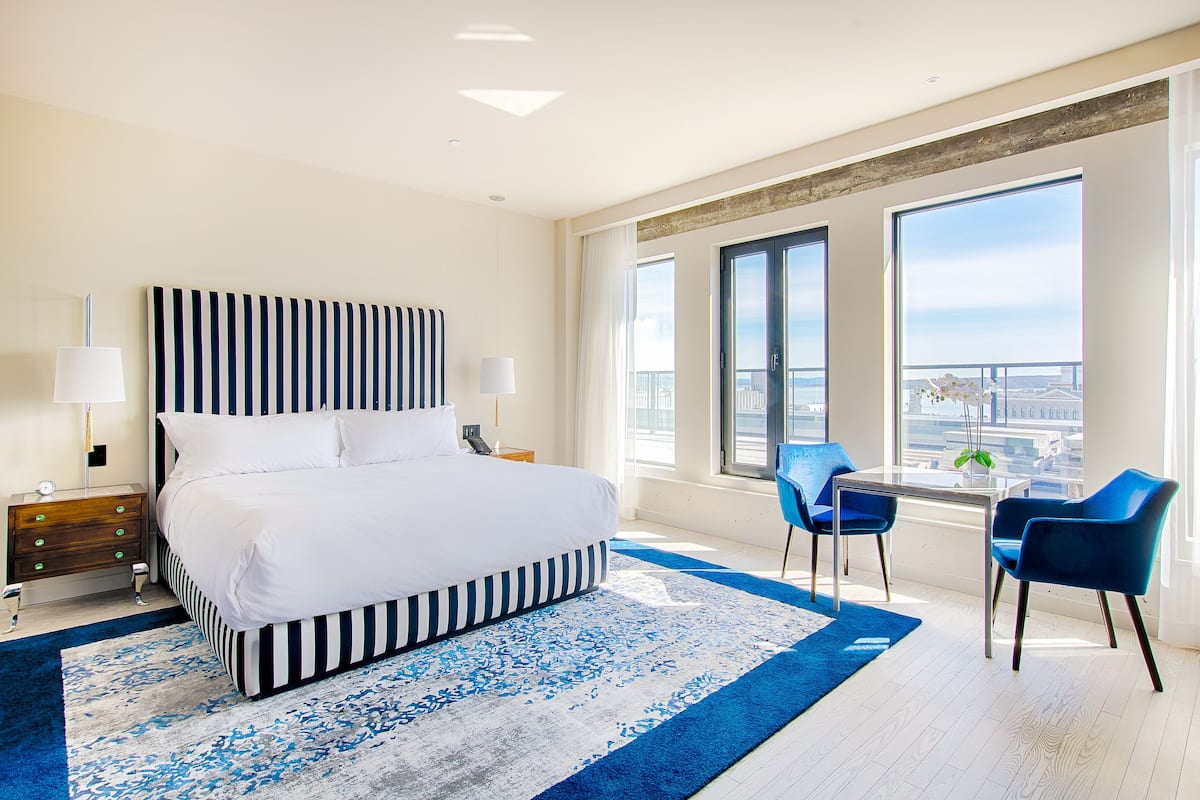 A modern hotel room with a large bed, a small table with chairs, and a balcony with a city view.