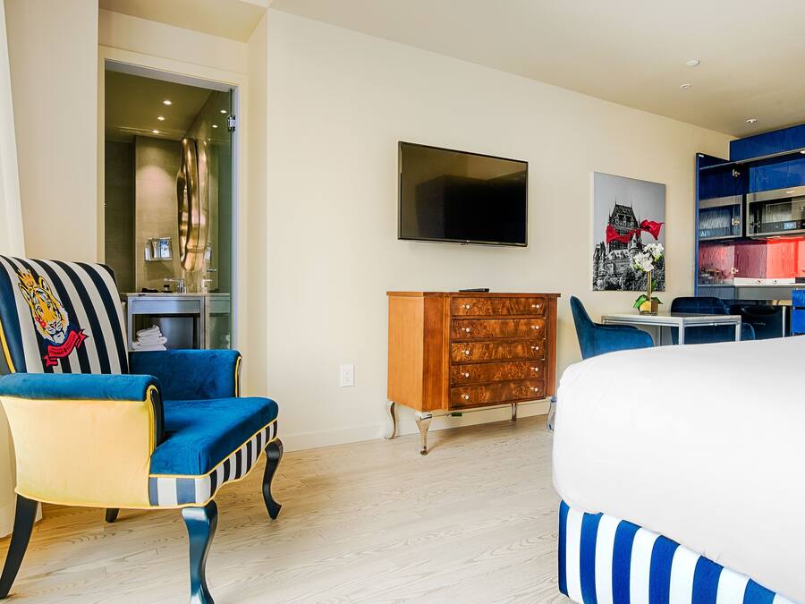 Una camera d'albergo moderna con un letto grande, una TV fissata al muro, un comò in legno e una poltrona a righe blu e bianche.