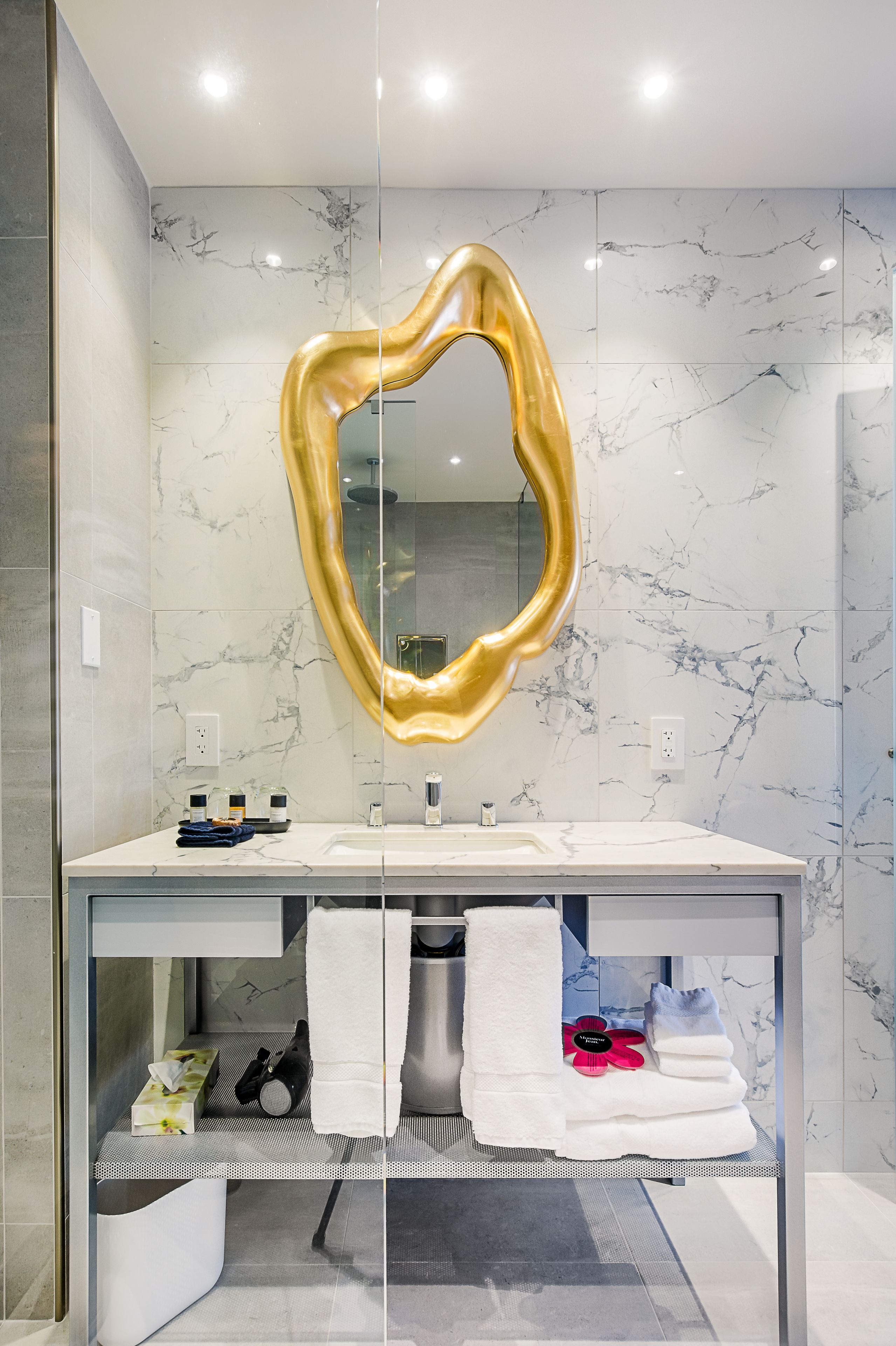A modern bathroom with a marble backsplash, a gold-framed mirror, and neatly arranged towels and toiletries.