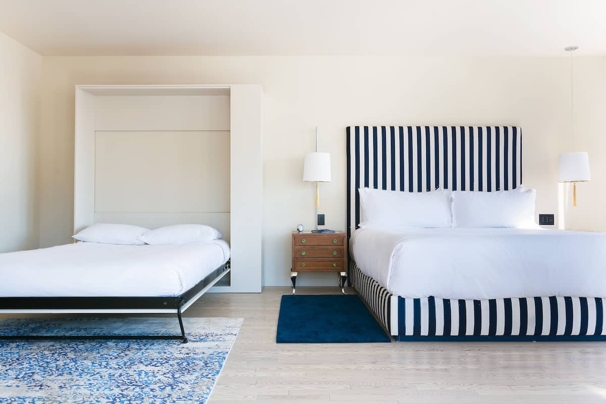 A hotel room with a bed, a nightstand, a lamp, and a door.