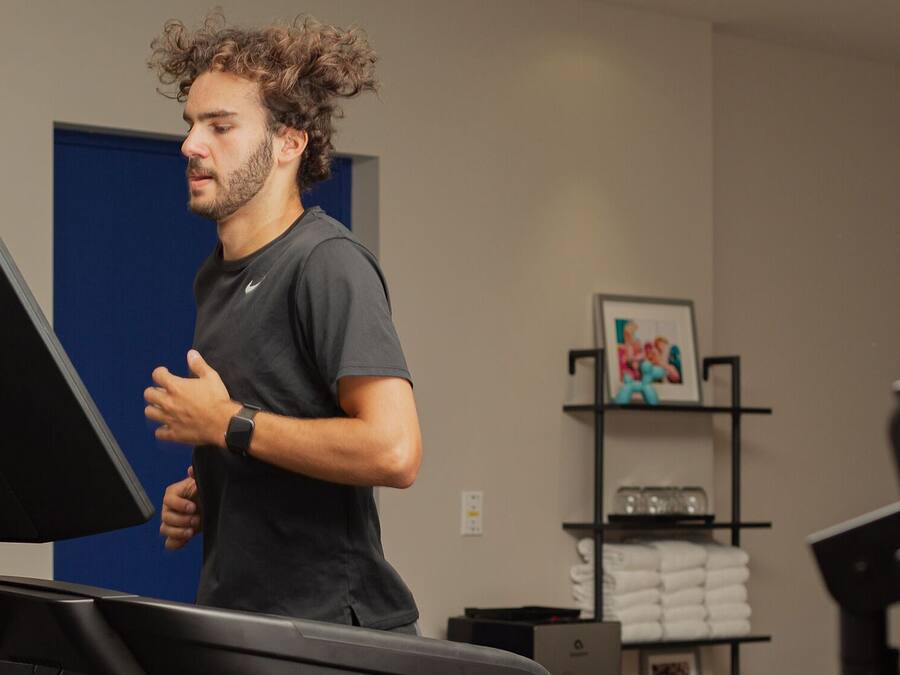 A man using a treadmill in a room with a blue door, a shelf with towels, and a framed picture on the wall.