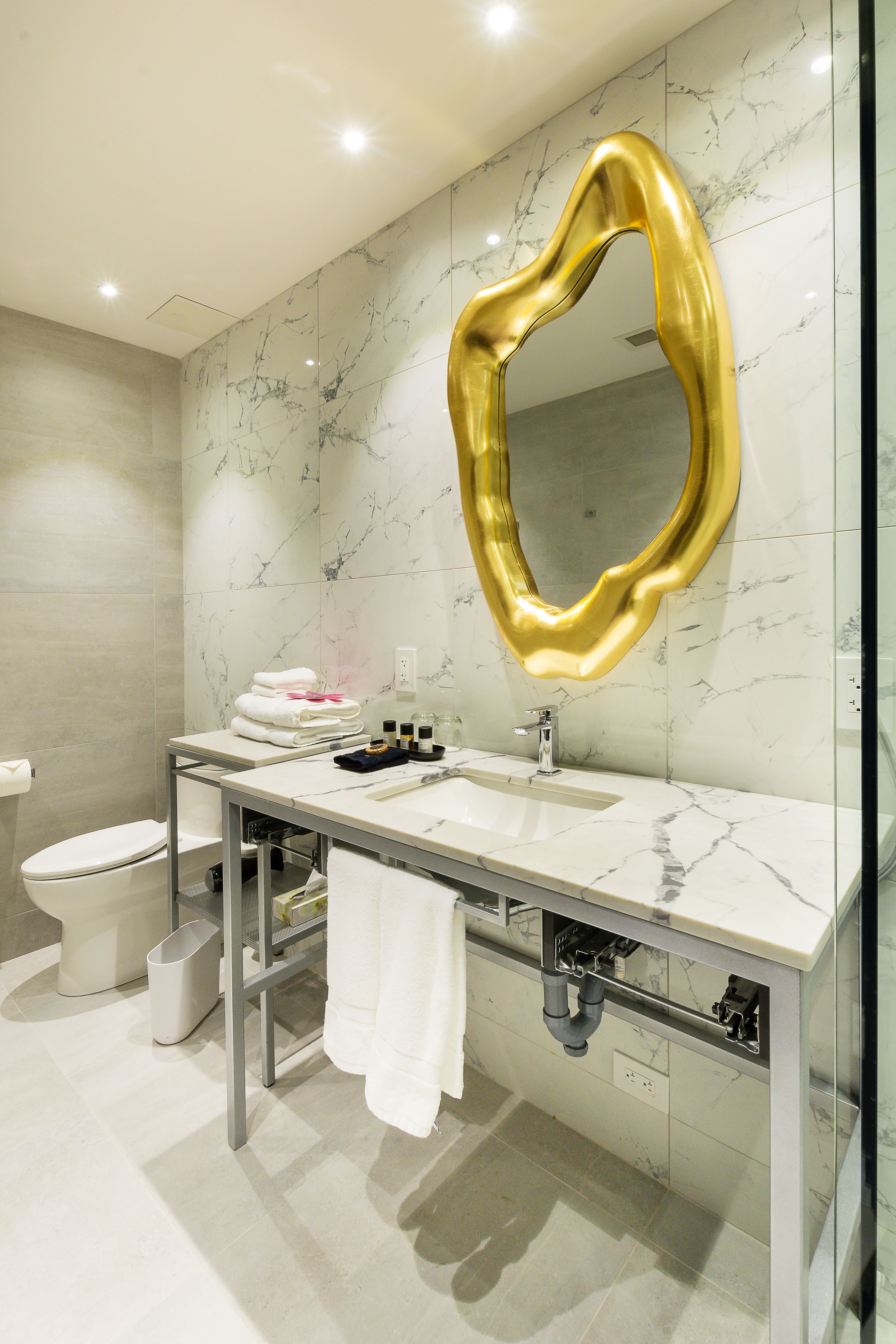 Un baño moderno con tocador de mármol, espejo con marco dorado y retrete blanco.