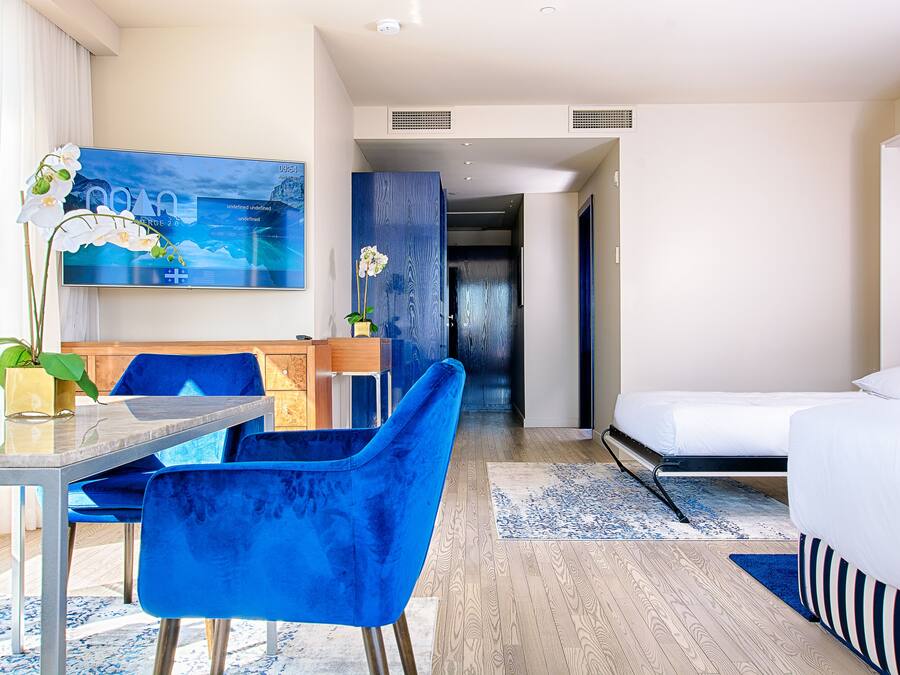Una habitación de hotel moderna con cama, escritorio con silla, televisor y una pared de acento azul.